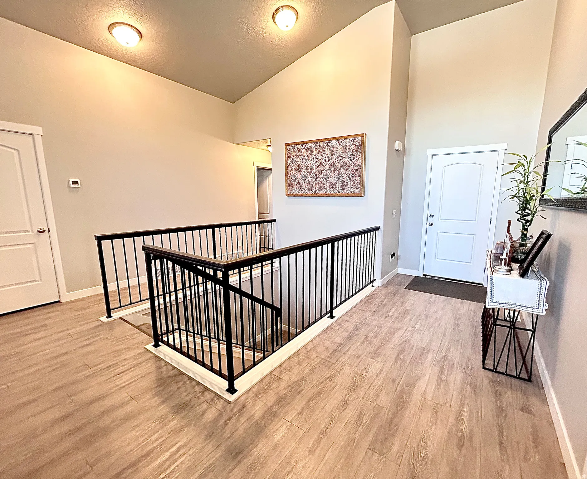 Hallway featuring an upstairs landing, light wood-style floors, a textured ceiling, and high vaulted ceiling