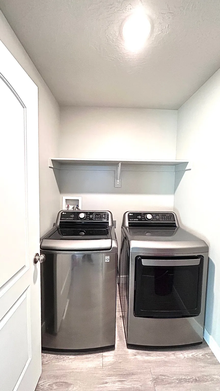Laundry room with a textured ceiling, light wood-type flooring, and washer and clothes dryer