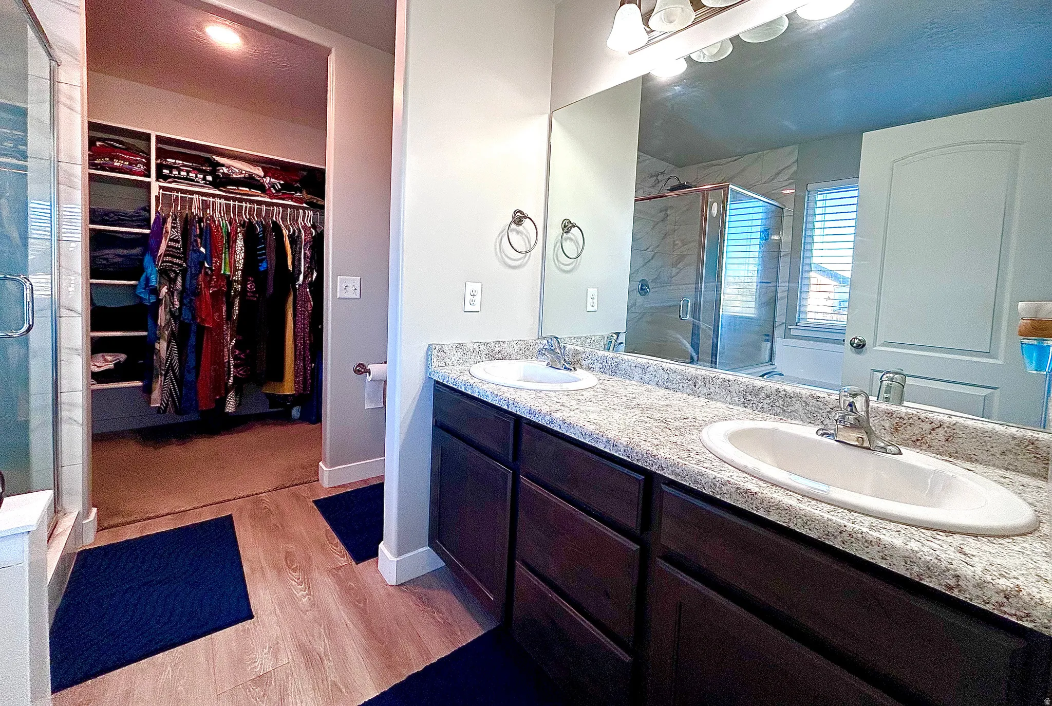 Bathroom with a stall shower, a spacious closet, double vanity, and light wood finished floors