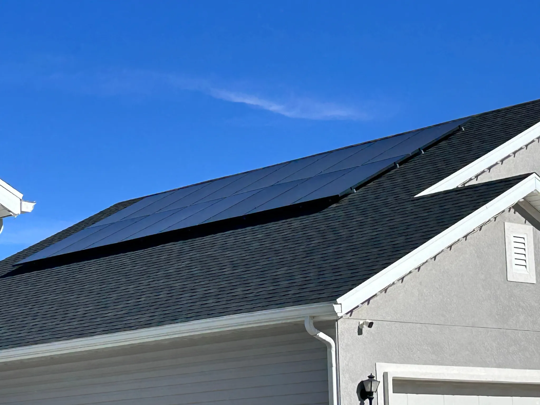 Exterior view of a shingled roof, a downspout, gutters, and stucco siding