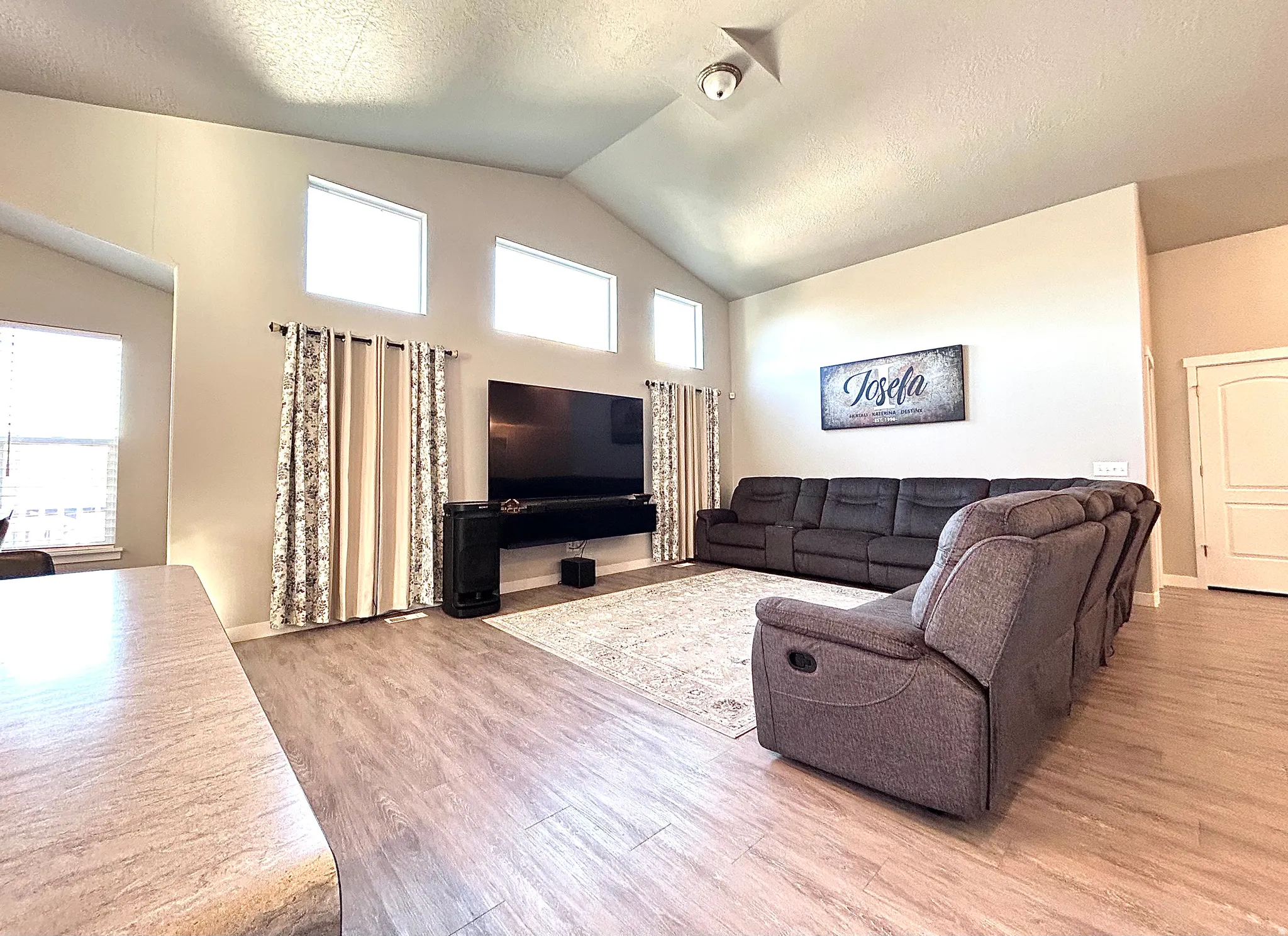 Living area featuring a textured ceiling, light wood-type flooring, and high vaulted ceiling