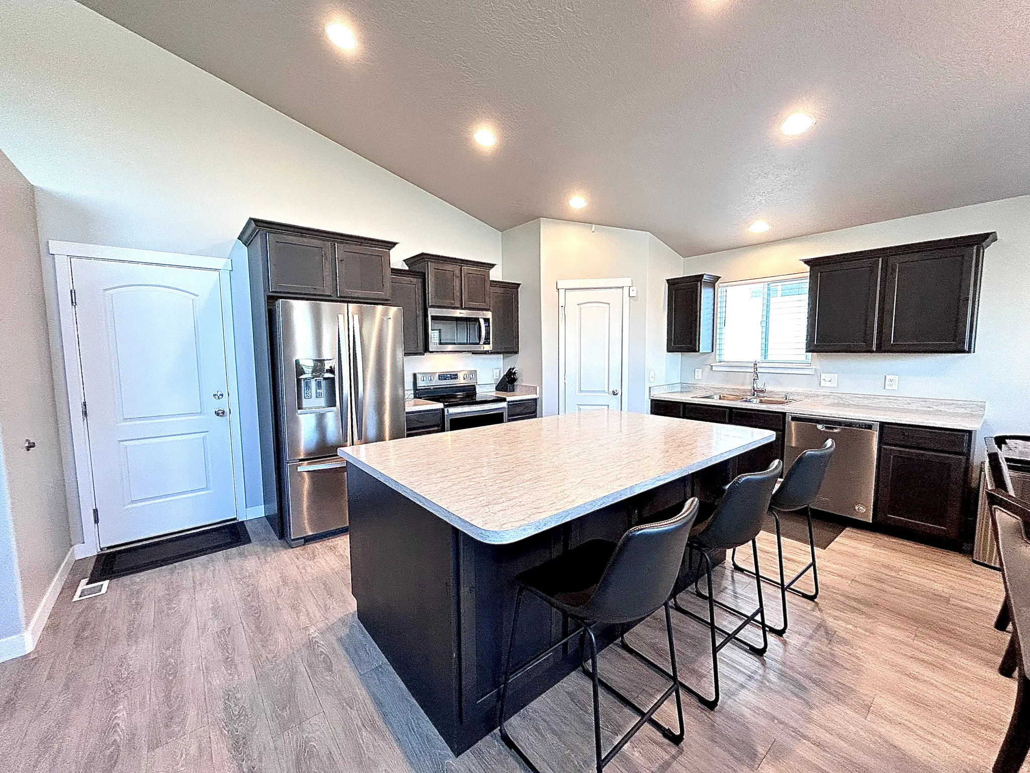 Kitchen featuring vaulted ceiling, stainless steel appliances, light countertops, a breakfast bar area, and light wood-type flooring