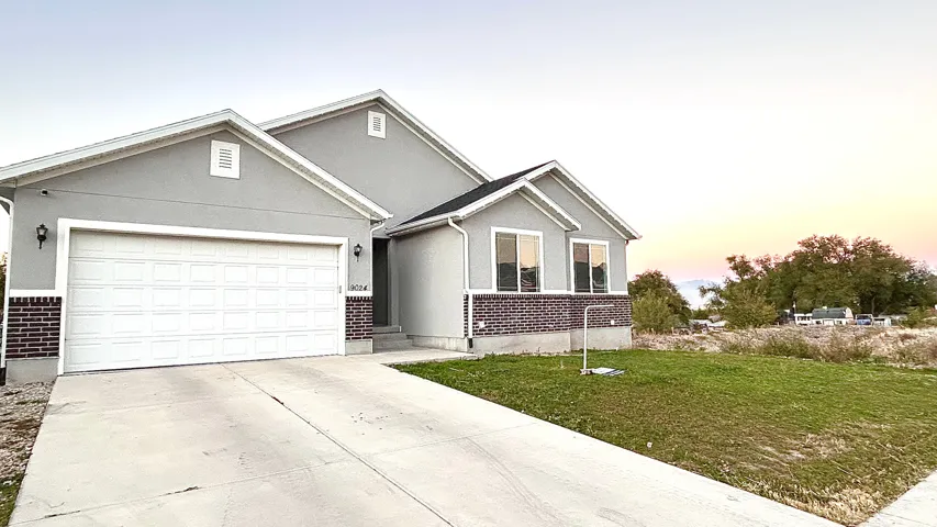 View of front of property with stucco siding, driveway, a lawn, brick siding, and an attached garage