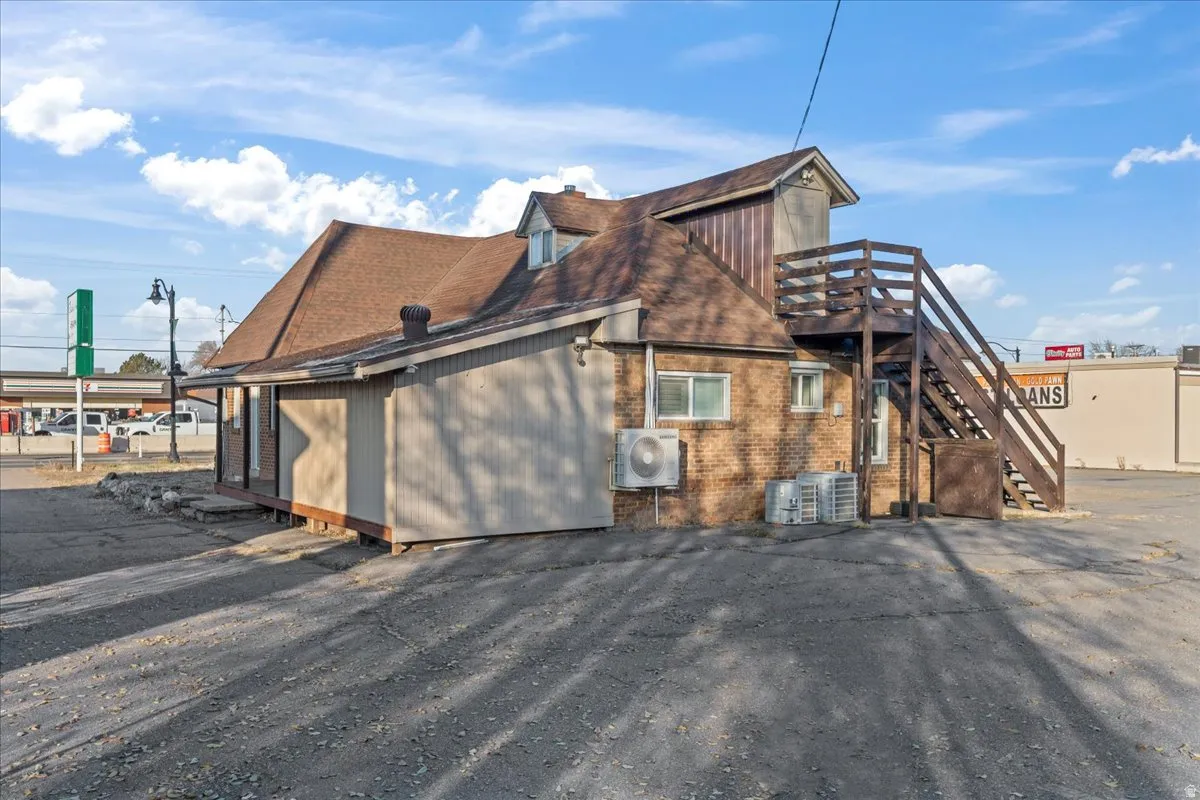 View of side of home featuring brick siding, stairs, and roof with shingles