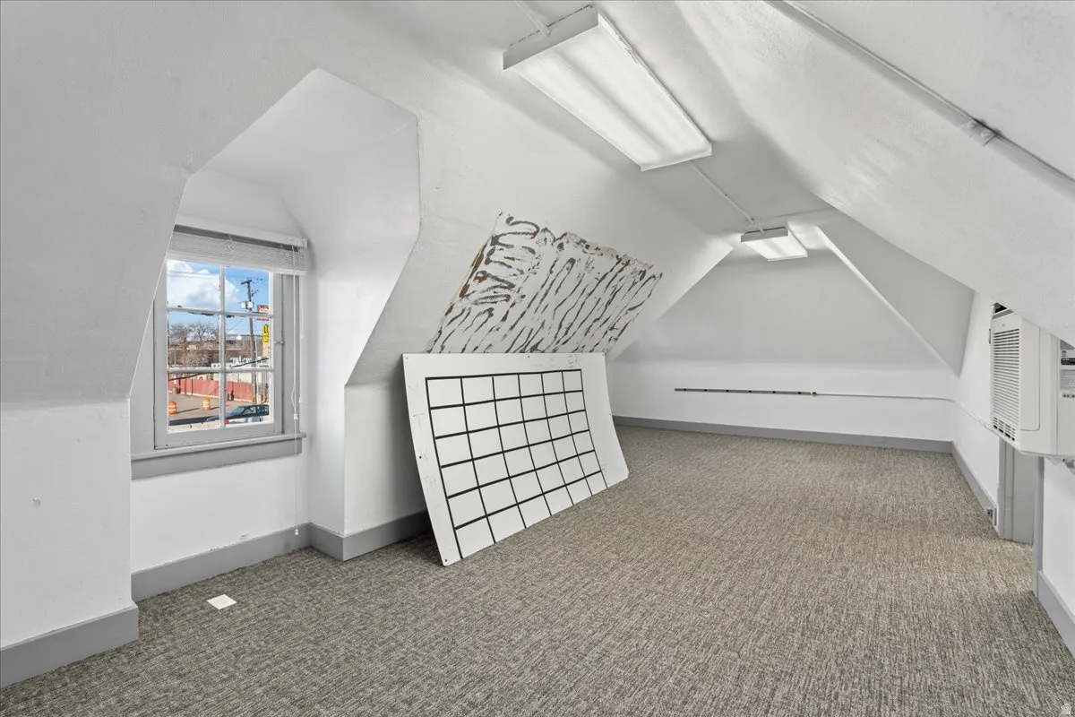 Additional living space featuring light carpet, lofted ceiling, and a wall unit AC