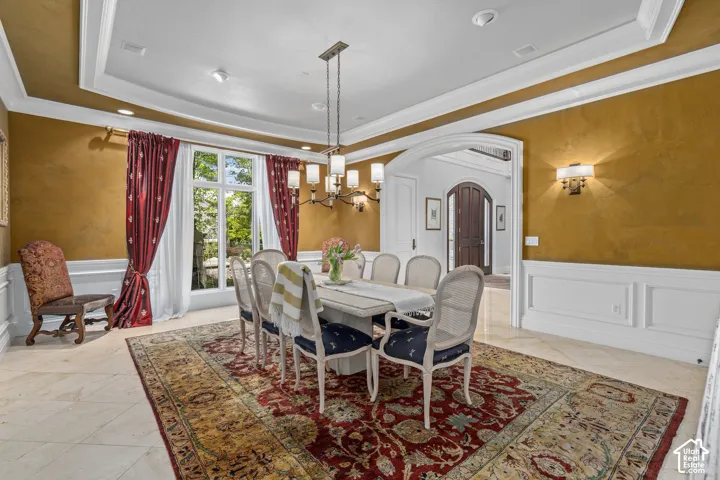 Dining area featuring wainscoting, a tray ceiling, arched walkways, a chandelier, and a decorative wall