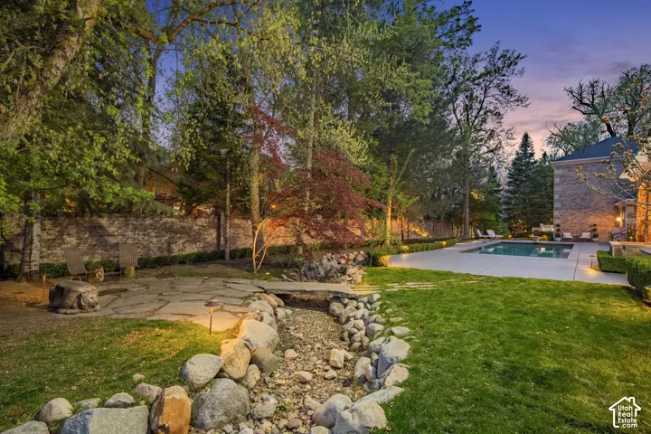 Yard at dusk with a patio, a lawn, and view of wooded area
