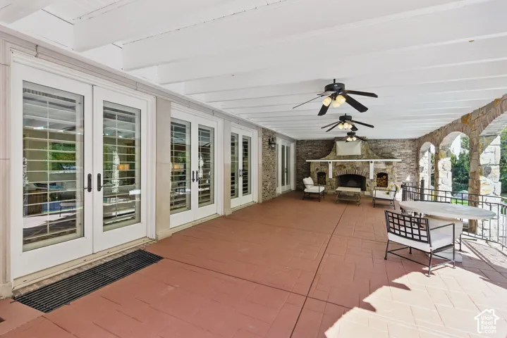 View of patio with a stone fireplace, a ceiling fan, outdoor dining space, and french doors