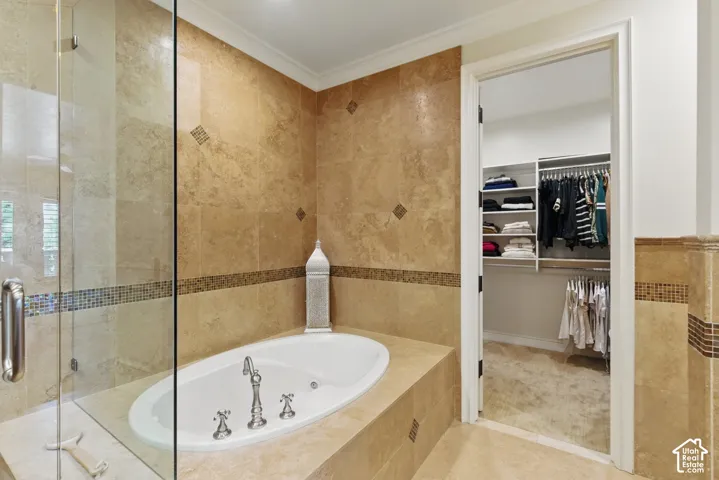 Bathroom featuring tile walls, a whirlpool tub, a walk in closet, crown molding, and a shower stall
