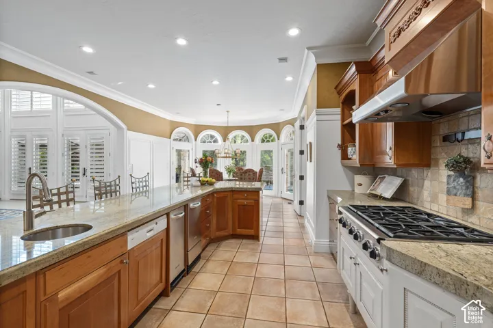 Kitchen featuring brown cabinets, crown molding, tasteful backsplash, exhaust hood, and stainless steel gas stovetop