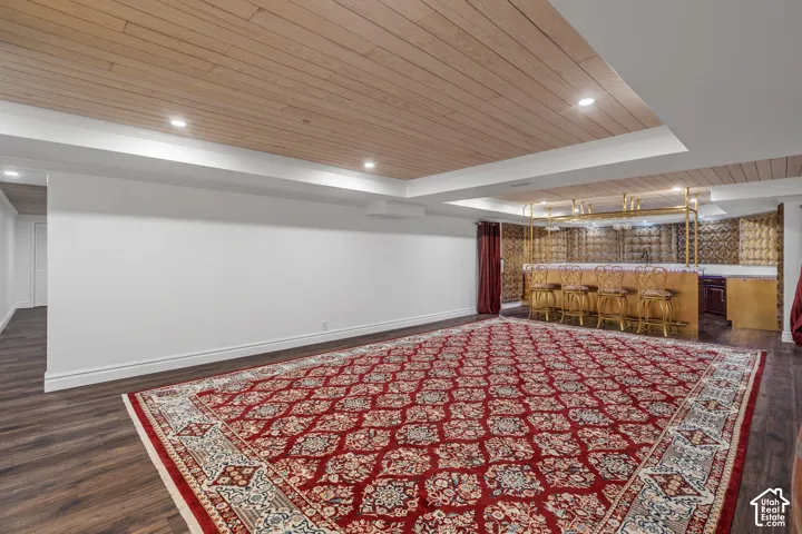 Finished basement featuring wooden ceiling, dark wood-style floors, recessed lighting, ornamental molding, and wet bar