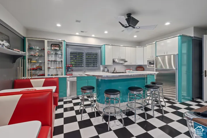Kitchen featuring dark flooring, light countertops, a kitchen bar, open shelves, and appliances with stainless steel finishes