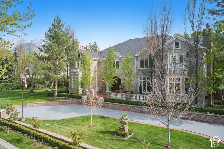 View of front of property featuring a front lawn, stone siding, a balcony, and a chimney