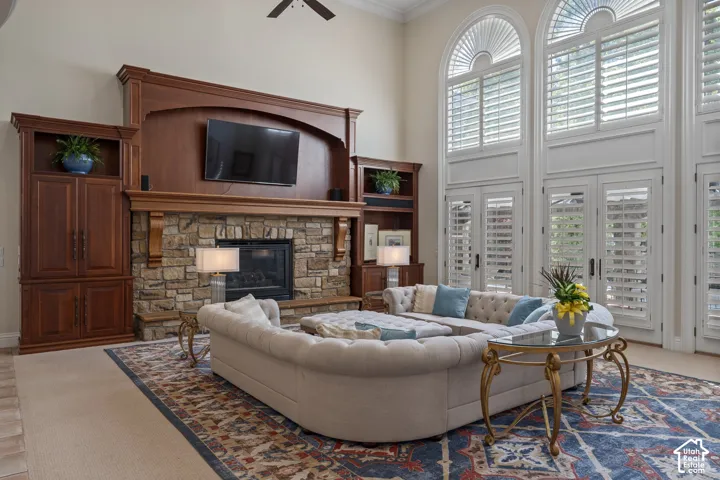 Living room featuring a stone fireplace, ornamental molding, a towering ceiling, carpet, and ceiling fan