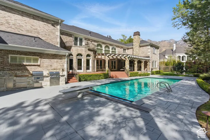 Outdoor pool with exterior kitchen, a patio area, a diving board, and a pergola