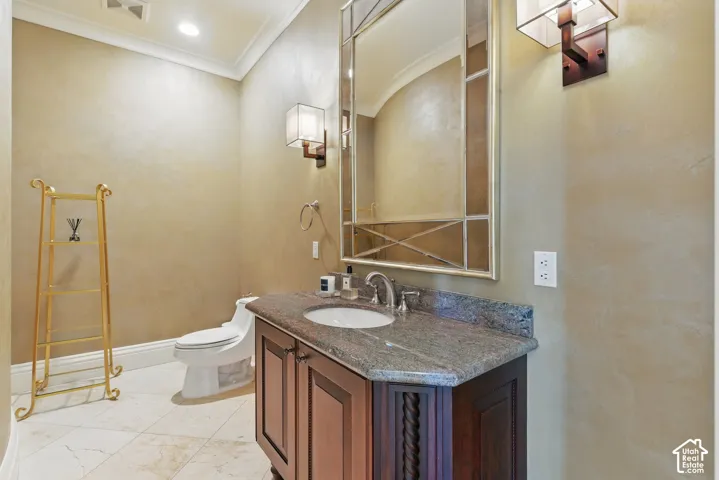 Half bathroom with vanity, crown molding, and light marble finish floors