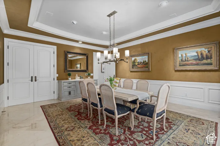 Dining room with a wainscoted wall, crown molding, a decorative wall, a chandelier, and a raised ceiling