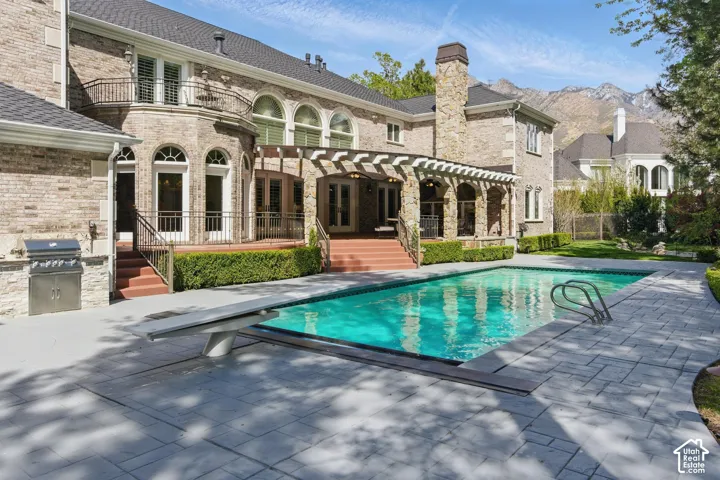 Rear view of house with a patio area, an outdoor pool, exterior kitchen, a balcony, and brick siding