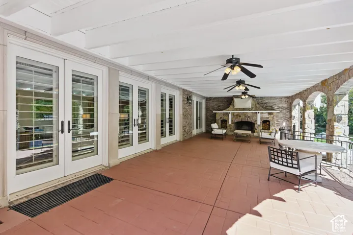View of patio featuring a stone fireplace, ceiling fan, outdoor dining area, and french doors