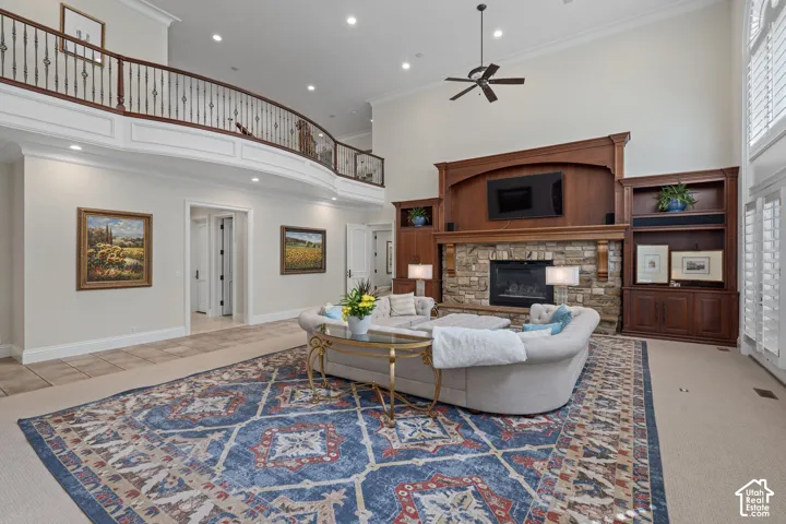 Living room with a towering ceiling, a stone fireplace, ornamental molding, recessed lighting, and a ceiling fan