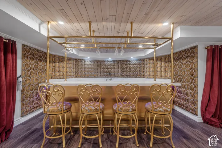 Indoor wet bar featuring dark wood finished floors, wooden ceiling, recessed lighting, brown cabinetry, and ornamental molding