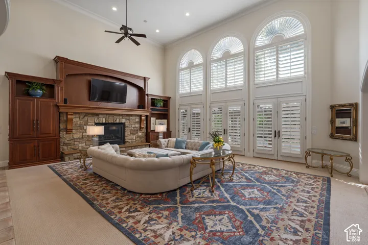 Carpeted living area featuring a high ceiling, a stone fireplace, ceiling fan, ornamental molding, and recessed lighting