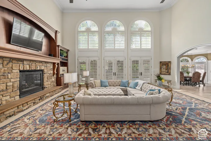Living area featuring ceiling fan, plenty of natural light, ornamental molding, a stone fireplace, and a high ceiling