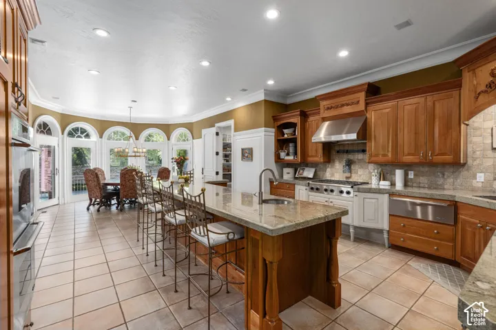 Kitchen featuring brown cabinetry, recessed lighting, ornamental molding, light tile patterned floors, and decorative backsplash
