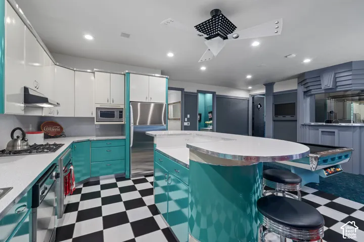 Kitchen with dark floors, a kitchen breakfast bar, white cabinetry, stainless steel appliances, and recessed lighting