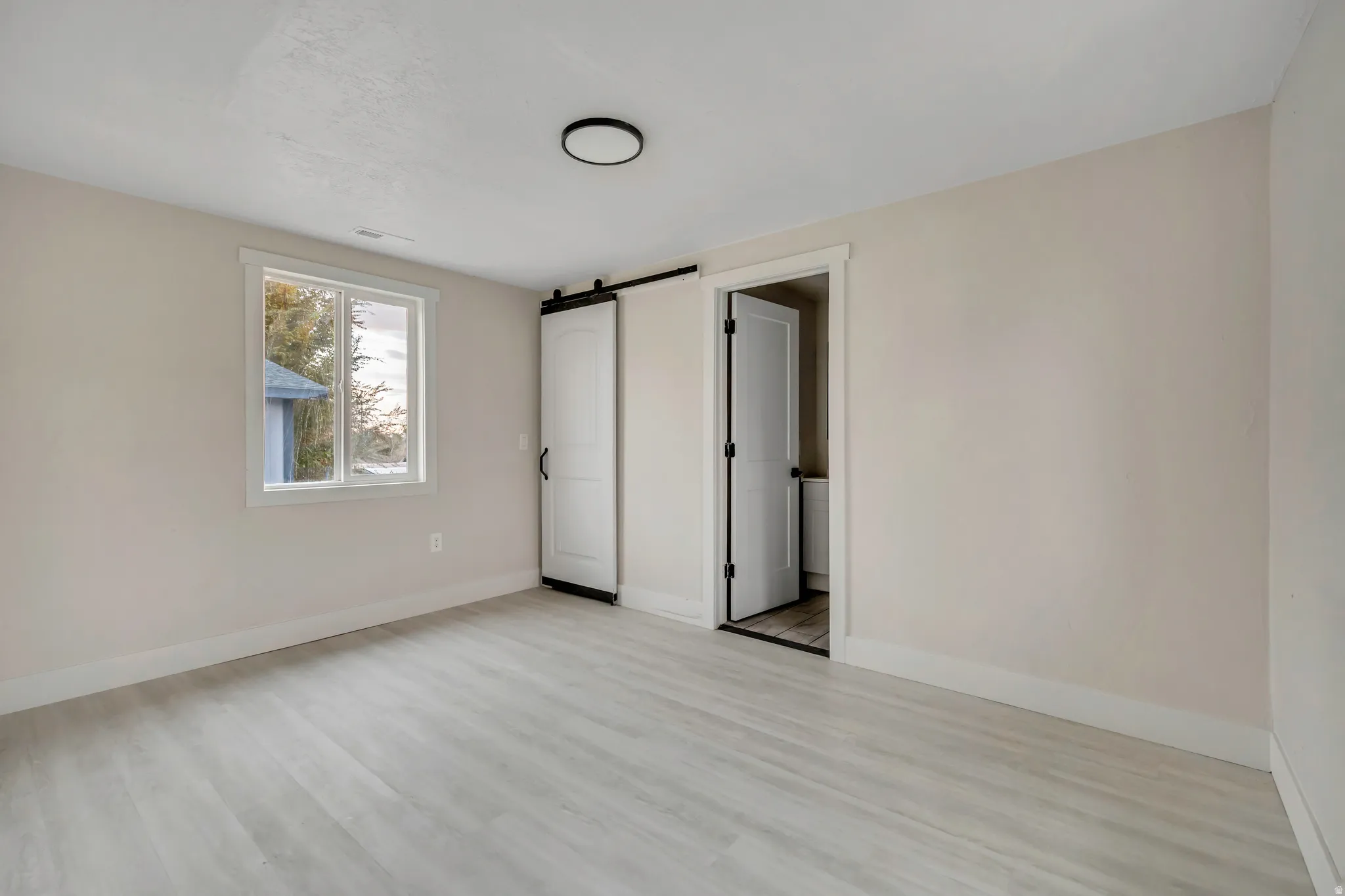 Unfurnished bedroom with a barn door and light wood finished floors