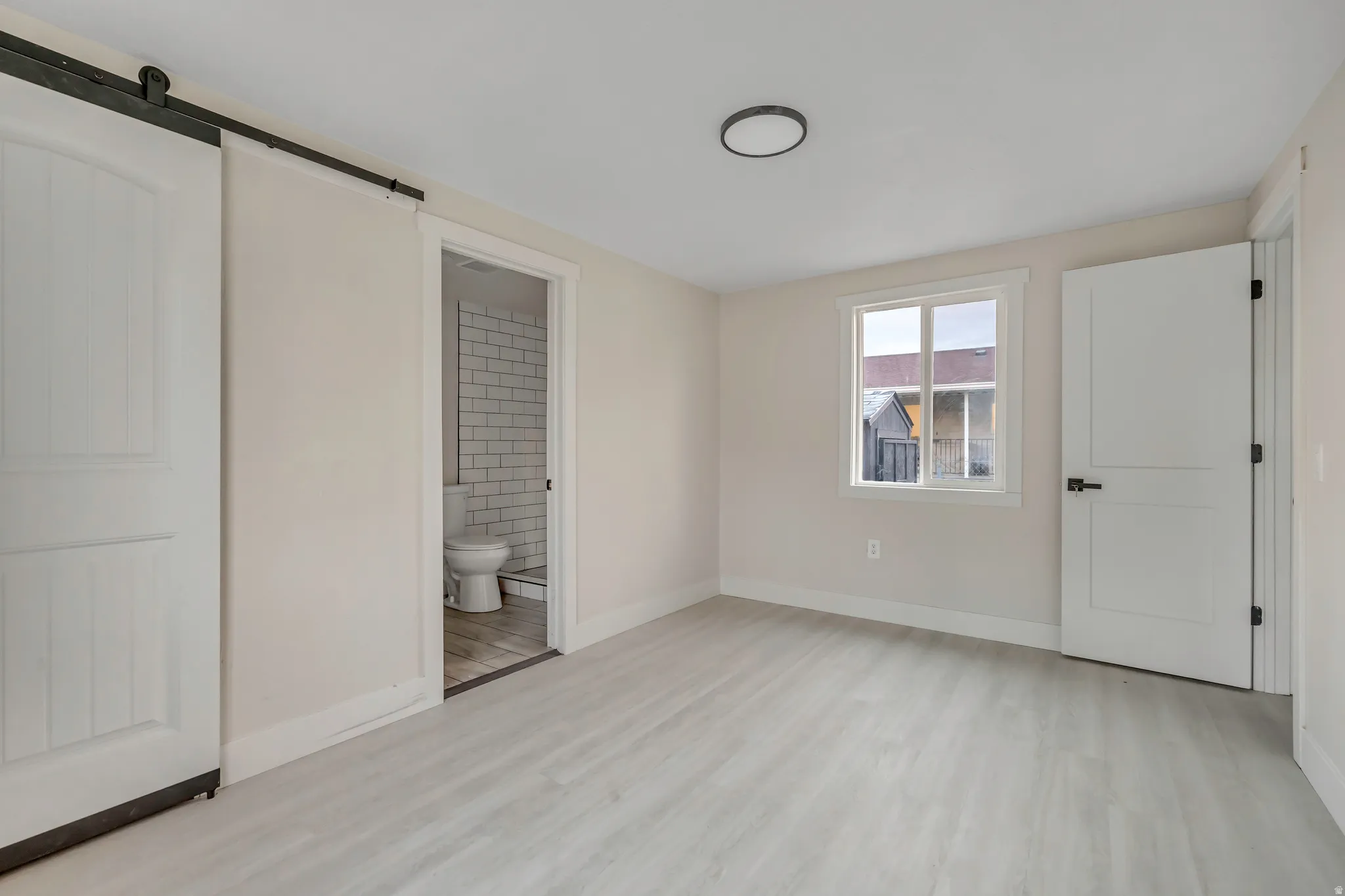 Unfurnished bedroom with a barn door, light wood-style floors, and ensuite bath