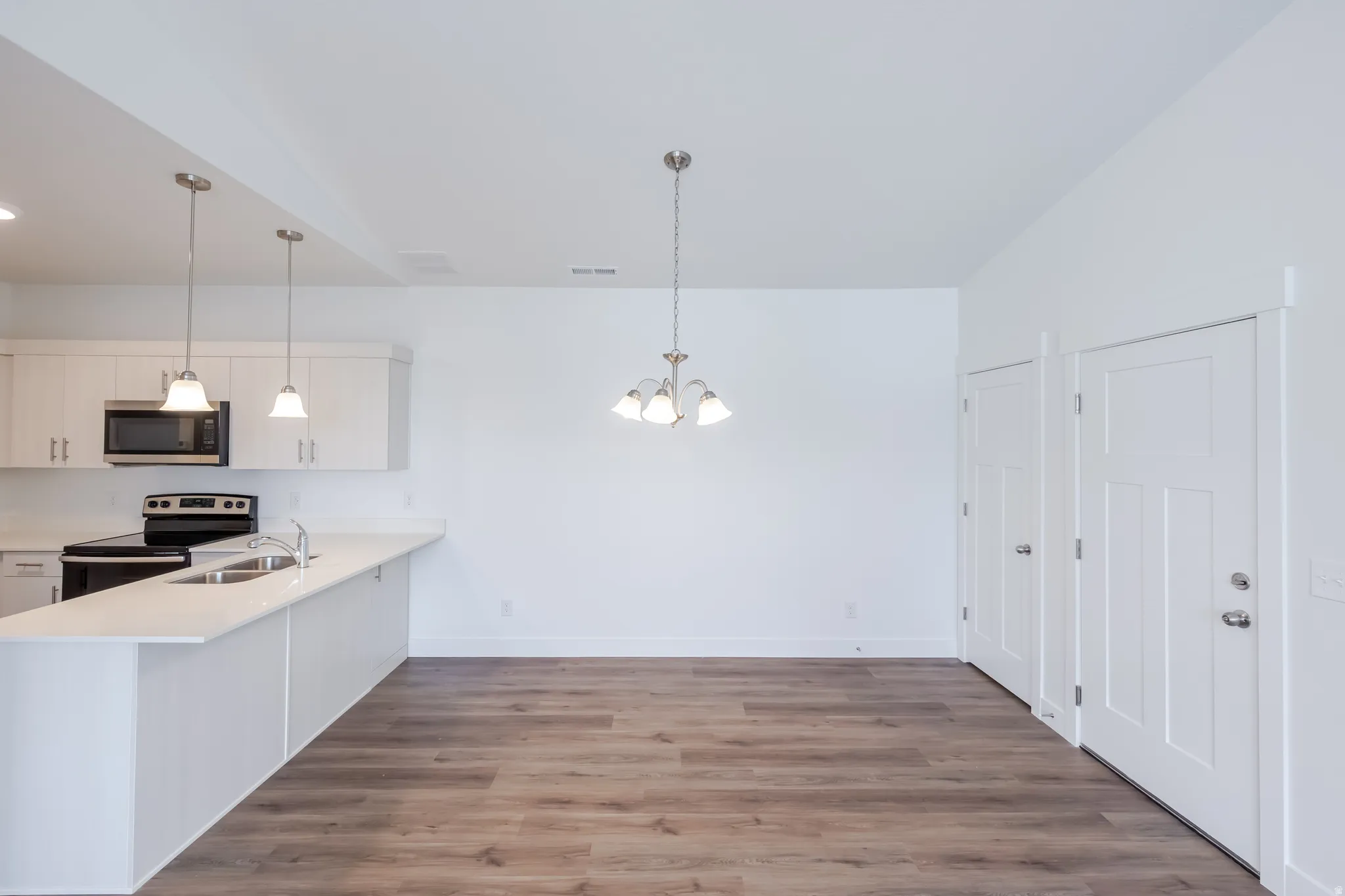 Kitchen with white cabinetry, a peninsula, stainless steel appliances, dark wood-type flooring, and a chandelier