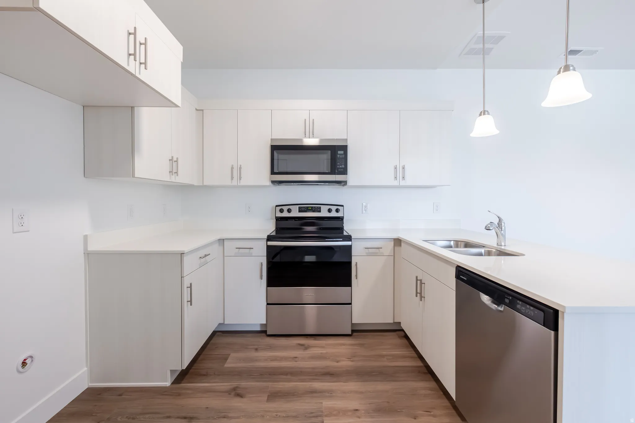 Kitchen featuring stainless steel appliances, a peninsula, dark wood-style floors, and pendant lighting