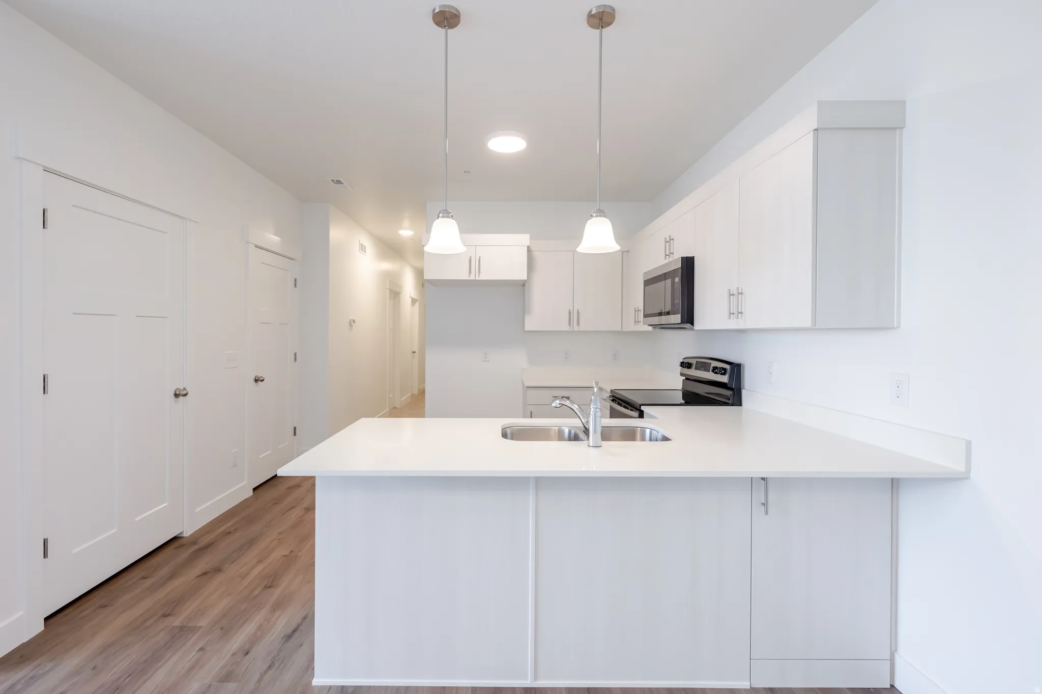 Kitchen with a peninsula, white cabinetry, hanging light fixtures, stainless steel appliances, and light wood-style flooring