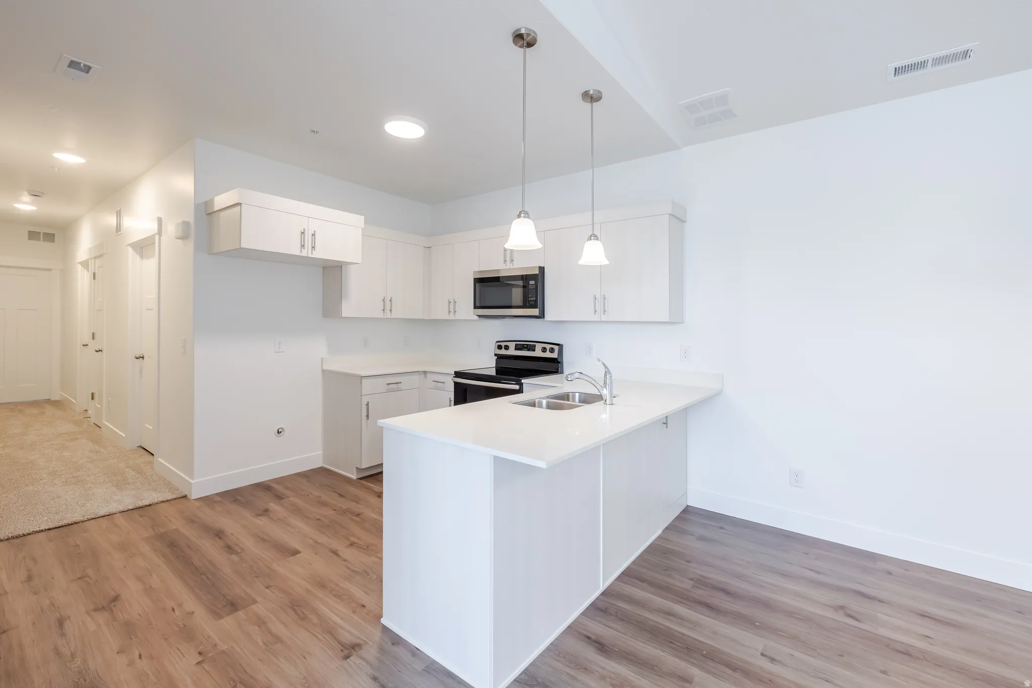 Kitchen with stainless steel appliances, a peninsula, pendant lighting, and light wood-type flooring