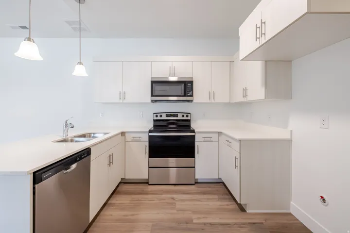 Kitchen featuring stainless steel appliances, a peninsula, light wood-type flooring, hanging light fixtures, and white cabinets