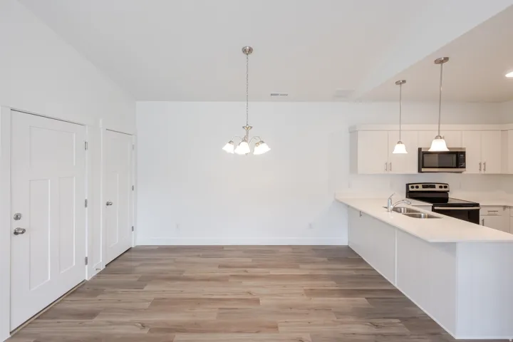 Kitchen with white cabinetry, a peninsula, electric stove, light wood-type flooring, and hanging lights