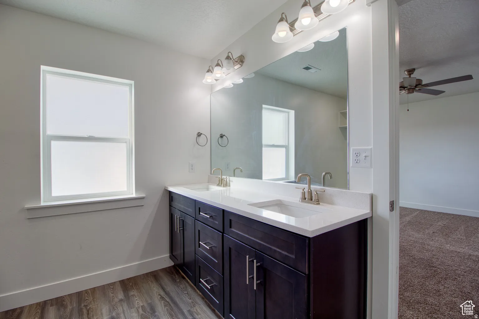 Bathroom featuring double vanity, ceiling fan, dark wood-type flooring, and a textured ceiling
