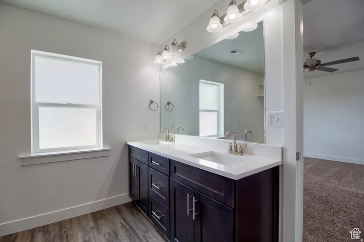 Bathroom featuring double vanity, ceiling fan, dark wood-type flooring, and a textured ceiling