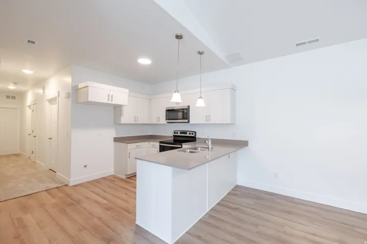 Kitchen with stainless steel appliances, light wood-style floors, a peninsula, and white cabinets