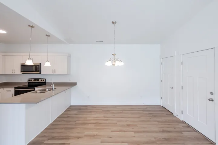 Kitchen with light wood-style floors, white cabinets, a peninsula, stainless steel appliances, and suspended lighting