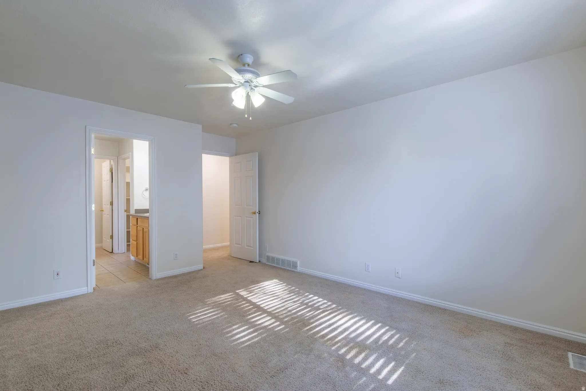 Unfurnished bedroom featuring light carpet, ensuite bath, and ceiling fan
