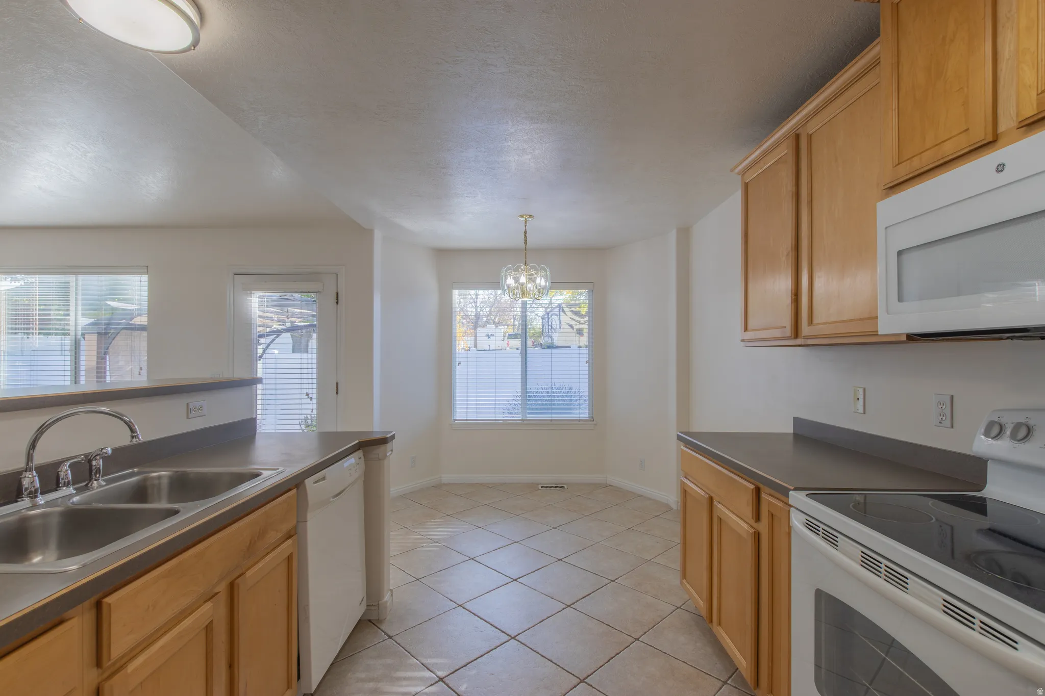 Kitchen featuring white appliances, dark countertops, light tile patterned floors, a chandelier, and decorative light fixtures