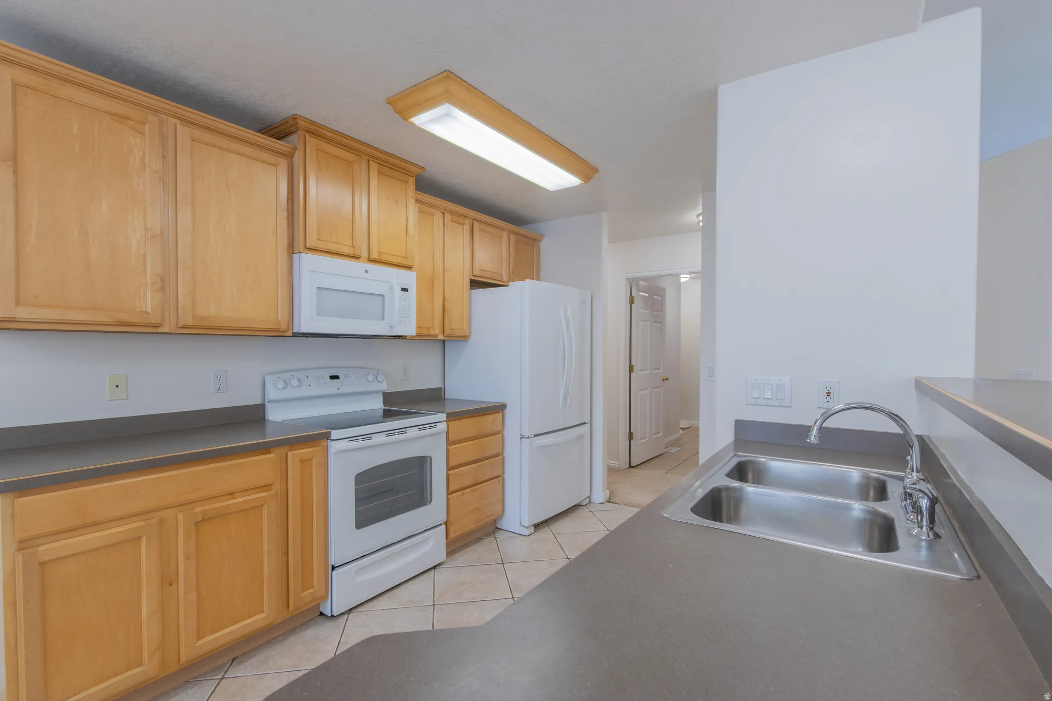 Kitchen featuring dark countertops, white appliances, light tile patterned flooring, and light brown cabinets