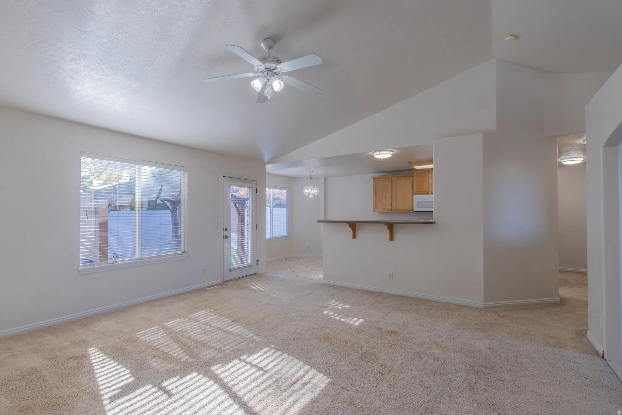 Unfurnished living room with light colored carpet, ceiling fan, and high vaulted ceiling