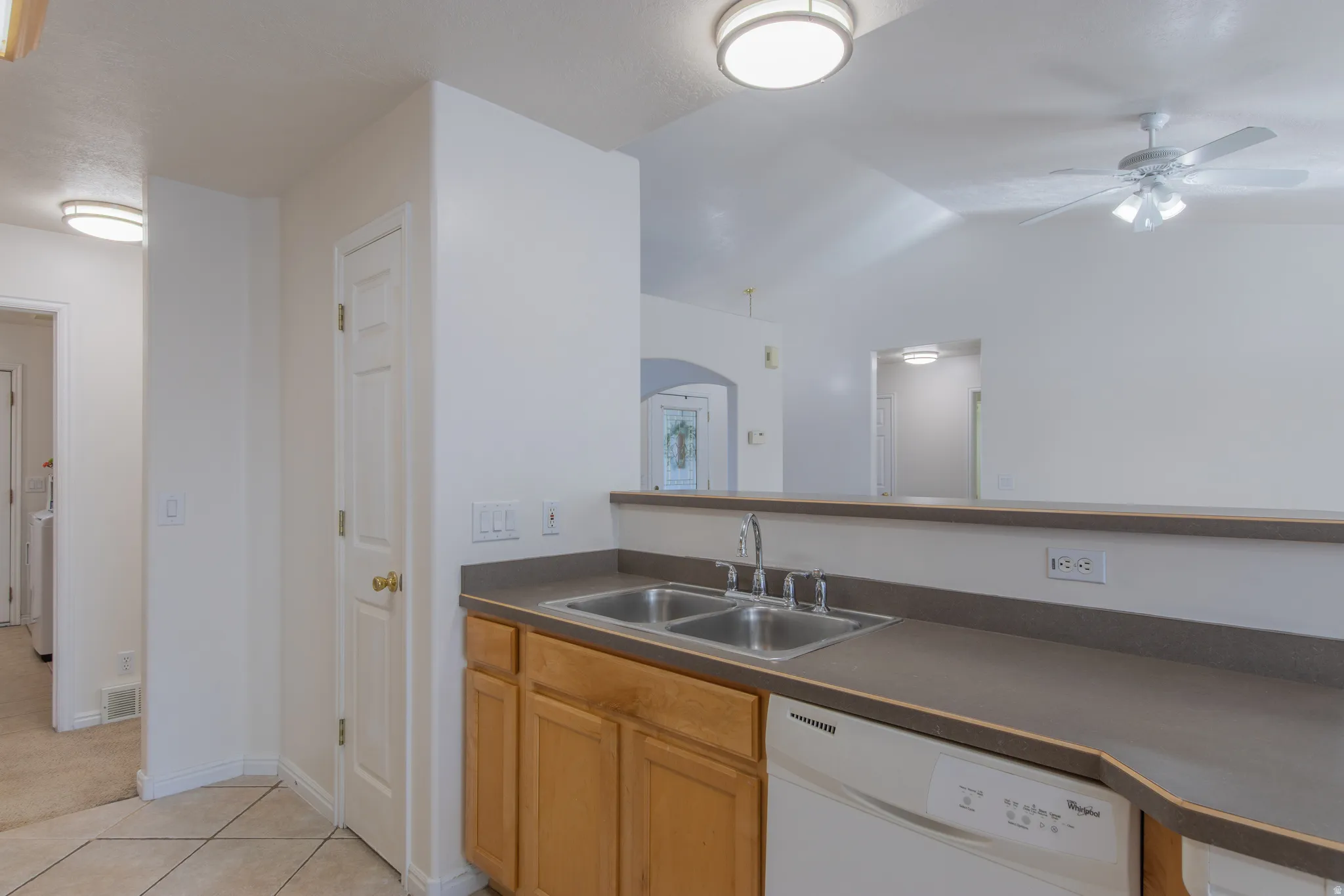Kitchen featuring dark countertops, dishwasher, light tile patterned flooring, ceiling fan, and lofted ceiling