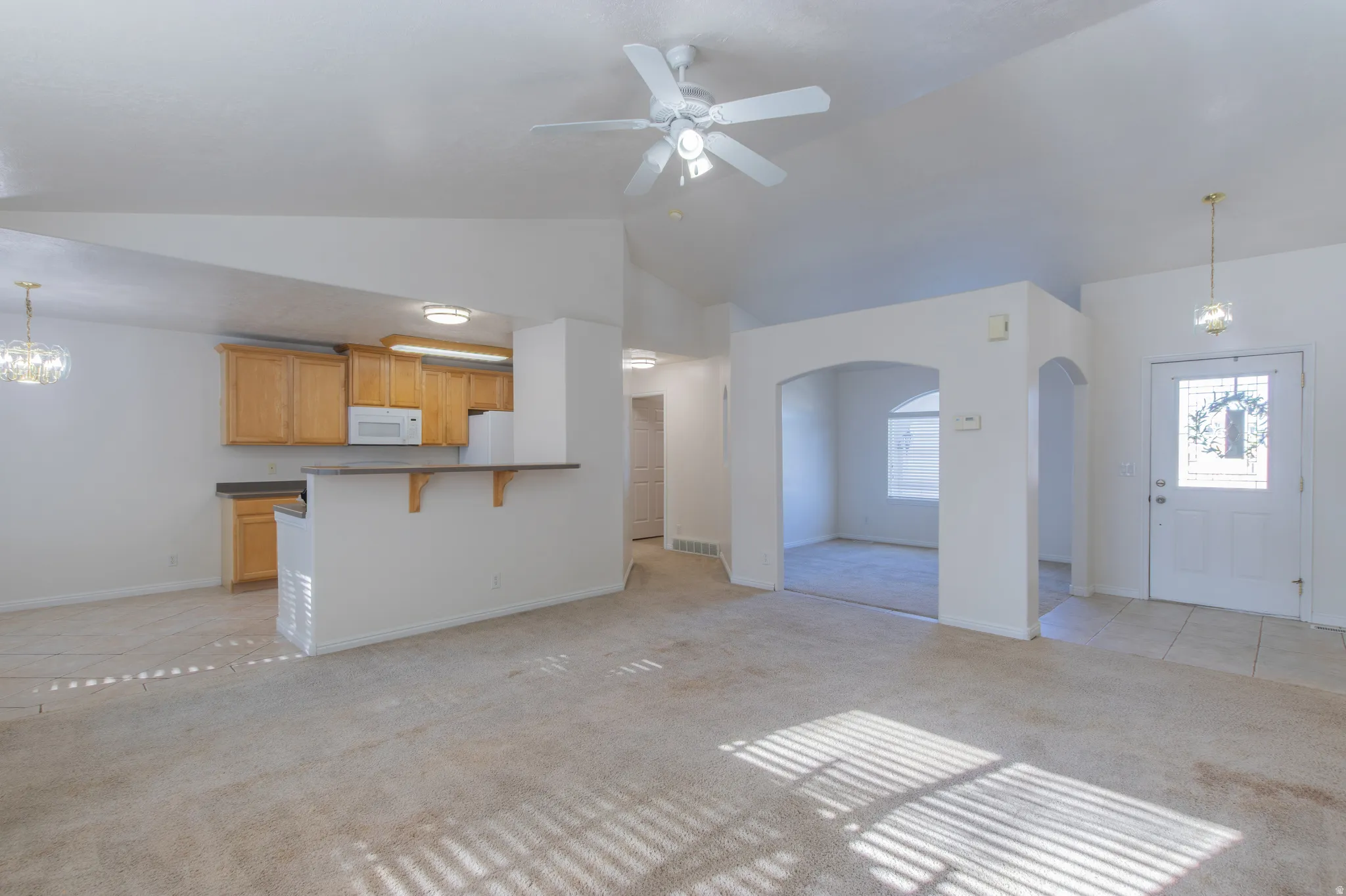 Unfurnished living room with a chandelier, light carpet, a ceiling fan, light tile patterned flooring, and high vaulted ceiling