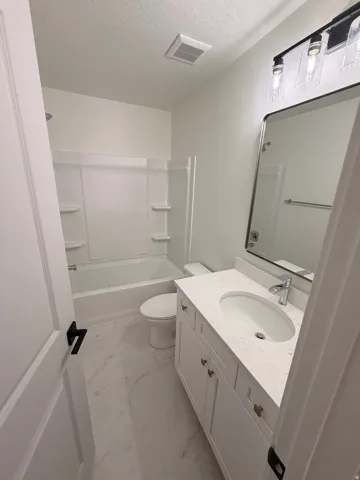 Full bath with vanity, light marble finish floors, shower / tub combination, and a textured ceiling