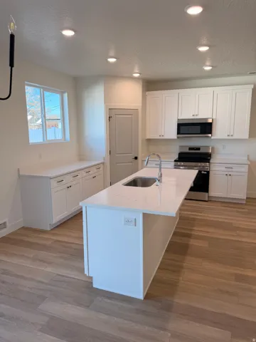 Kitchen featuring white cabinets, stainless steel appliances, light stone counters, a center island with sink, and a textured ceiling