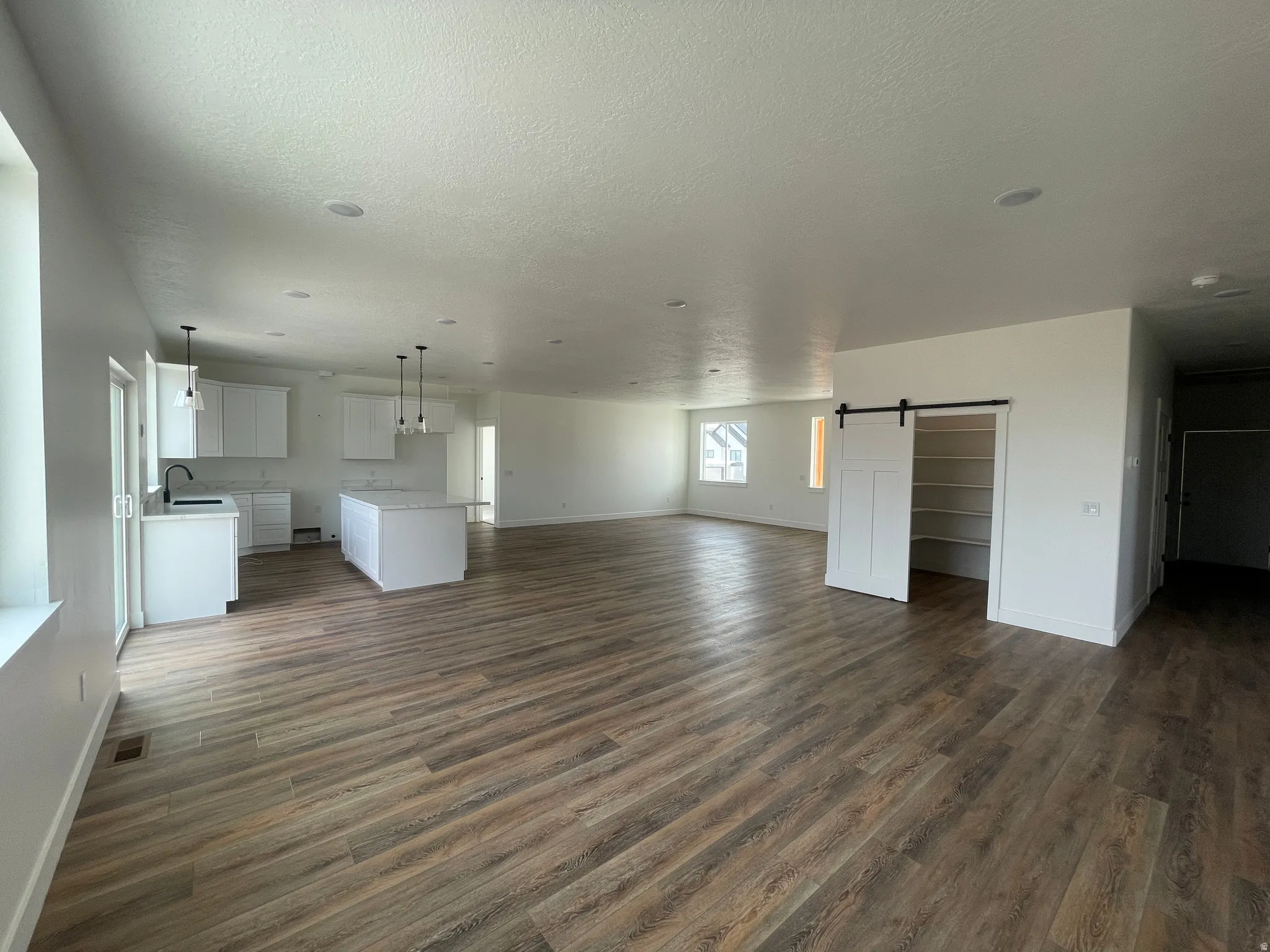 Unfurnished living room with a barn door, dark wood-style floors, and a textured ceiling